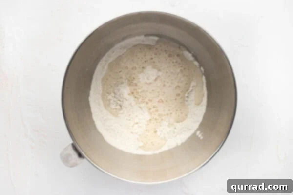 Flour and salt in a stand mixer bowl, with bloomed yeast mixture being added.
