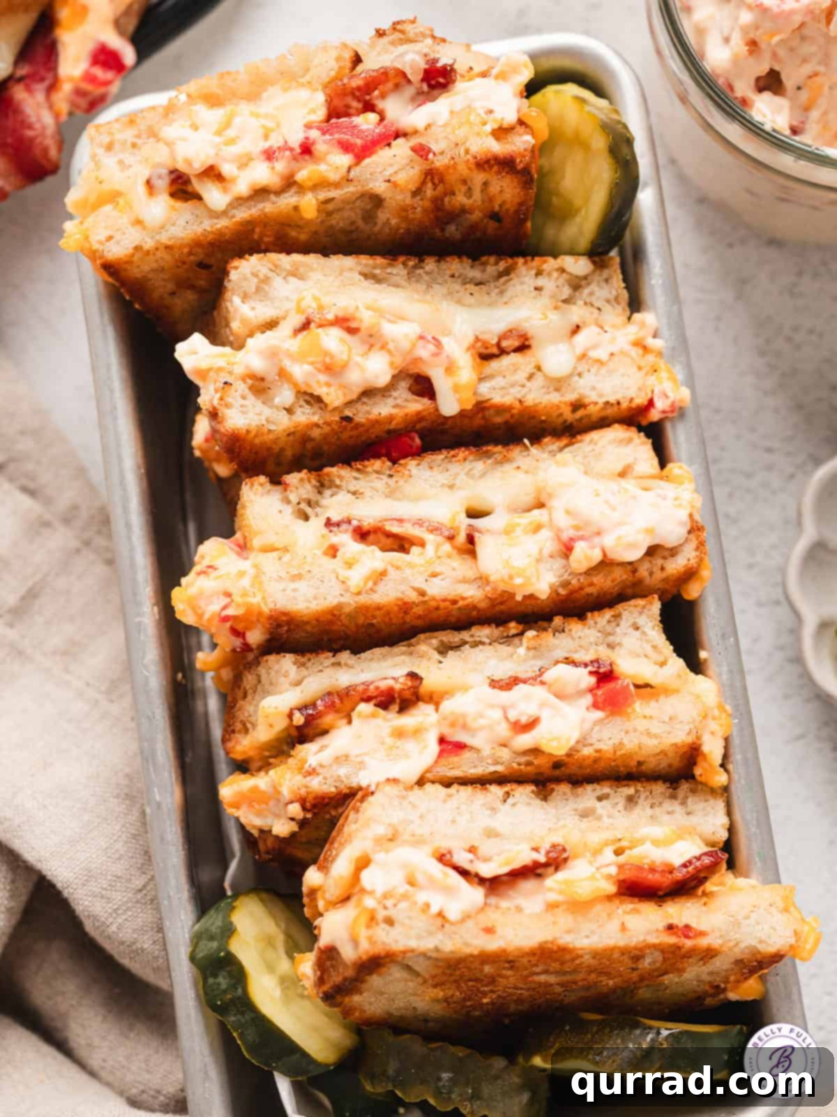 Two halves of a Pimento Grilled Cheese sandwich artfully arranged, showcasing the perfect melt of provolone and creamy pimento cheese with crispy bacon.