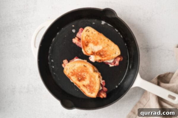 Two pimento grilled cheese sandwiches sizzling in a cast iron skillet, cooking to a golden perfection.