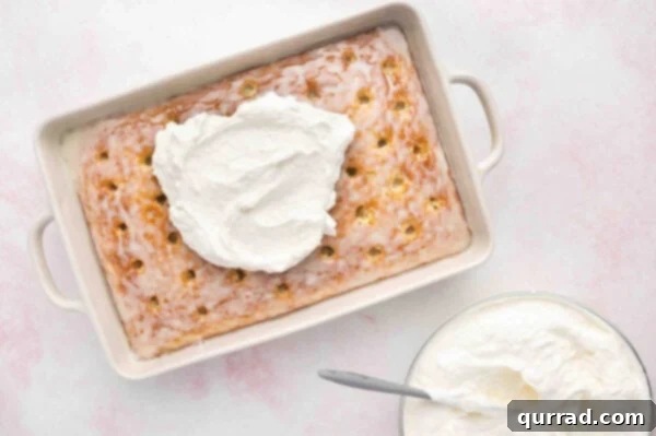 The coconut whipped topping being spread smoothly over the infused baked cake in the pan.
