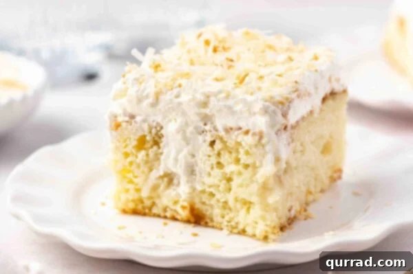 A perfect square slice of frosted coconut cake on a white plate, ready to be enjoyed.