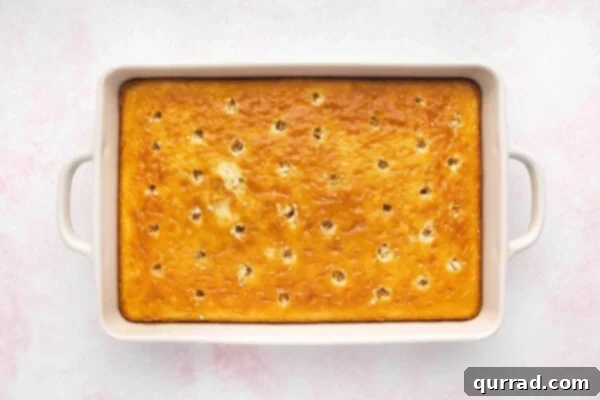 A baked cake in a casserole dish with many small holes poked uniformly across its surface.