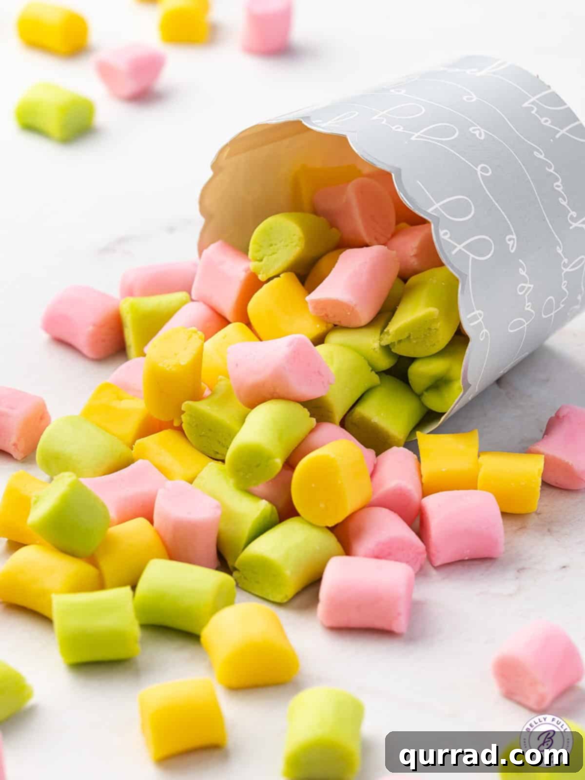 Butter mints of various pastel colors spilling attractively from a small paper cup, highlighting their delightful presentation.