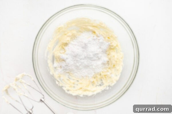Powdered sugar being added to creamed butter mixture in a bowl