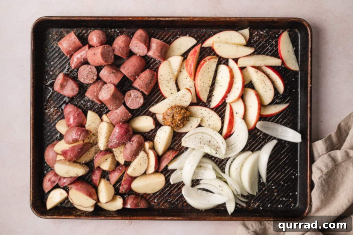 Harvest Sheet Pan Sausage and Apple Dinner 3 Chicken sausage, quartered baby new potatoes, sweet onion wedges, and sliced Honeycrisp apple pieces arranged on a baking sheet, ready for seasoning.