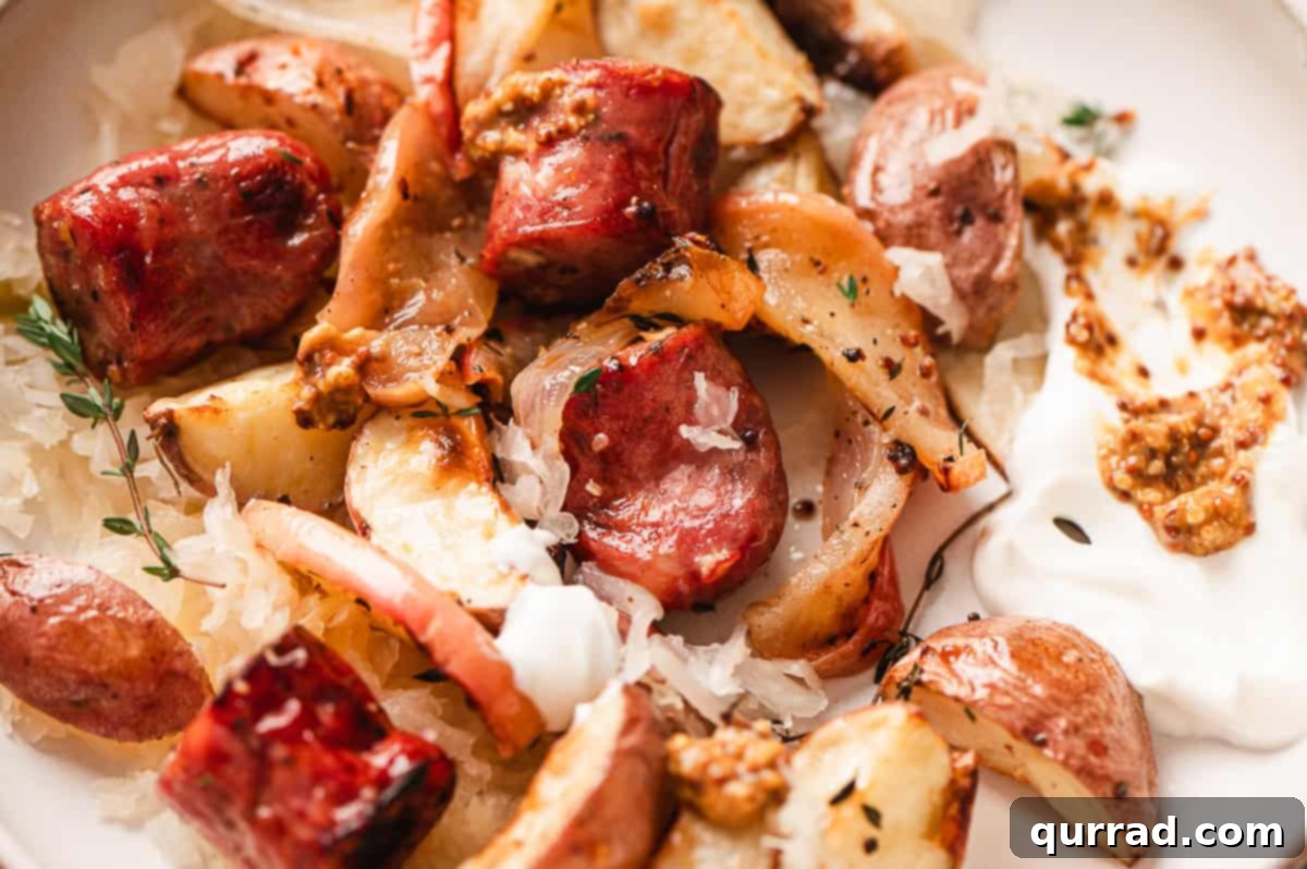 Harvest Sheet Pan Sausage and Apple Dinner 6 A close-up of a single serving of the roasted sheet pan potato, apple, and sausage dinner on a plate, garnished with a dollop of sour cream and a side of sauerkraut, ready to be enjoyed.
