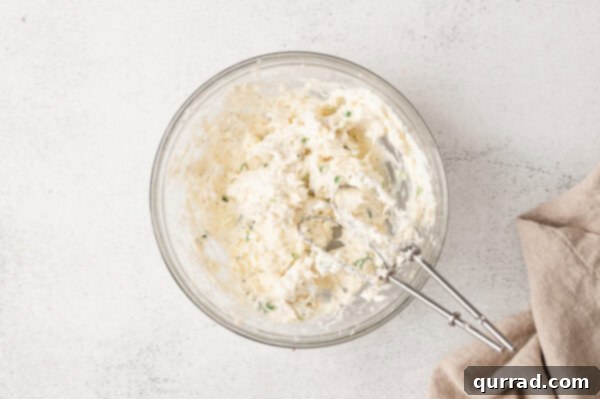 Loaded Baked Potato Delights 7 A whipped cream cheese in a glass mixing bowl with a hand mixer.