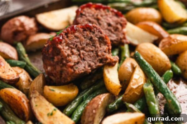 A mini meatloaf cut in half on a plate of potatoes and green beans, ready to serve