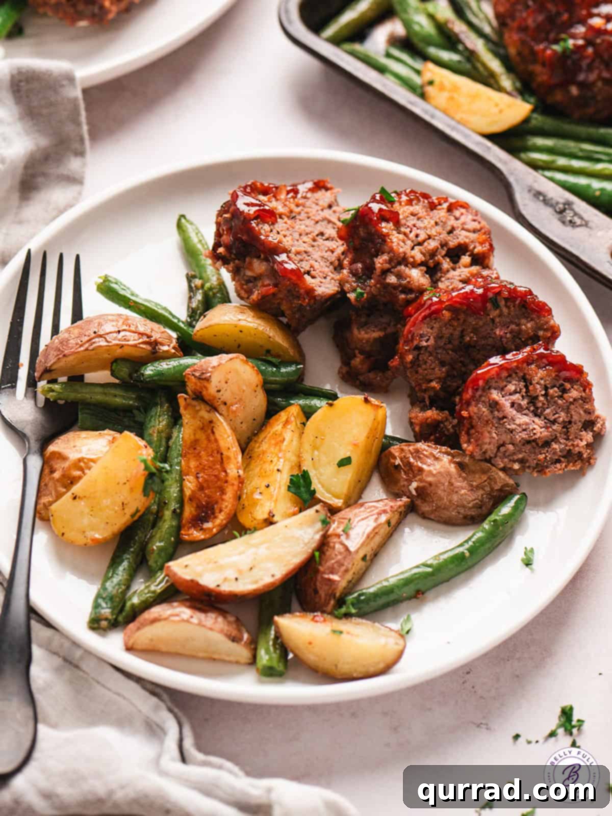 Sliced Mini Meatloaf with Perfectly Roasted Vegetables A sliced mini meatloaf on a plate with roasted potatoes and green beans, showcasing the moist interior