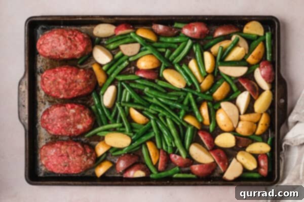 Overhead view of unbaked mini meatloaves, green beans, and potatoes arranged on a baking sheet