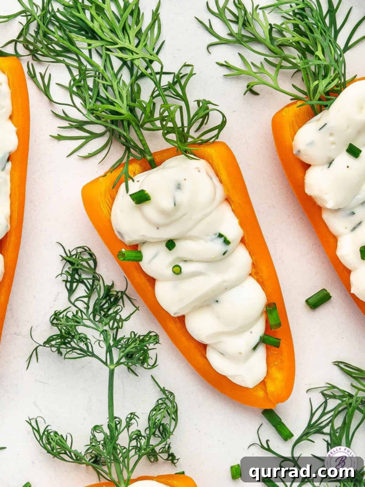 Crunchy orange mini peppers are stuffed with an herb-infused cream cheese mixture in these Stuffed Mini Bell Pepper Carrots. Close up of stuffed mini bell pepper carrots arranged on a serving plate