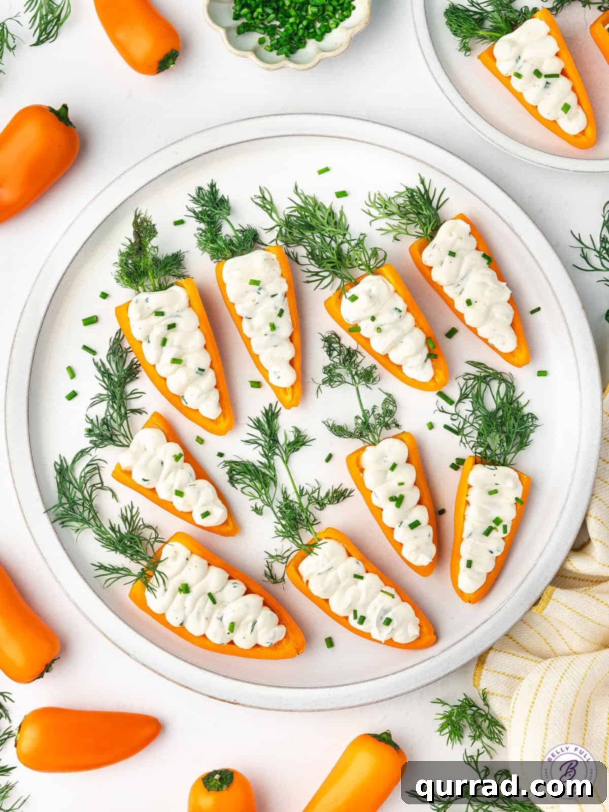 Crunchy orange mini peppers are stuffed with an herb-infused cream cheese mixture in these Stuffed Mini Bell Pepper Carrots. Stuffed mini bell pepper carrots on a white plate, close-up