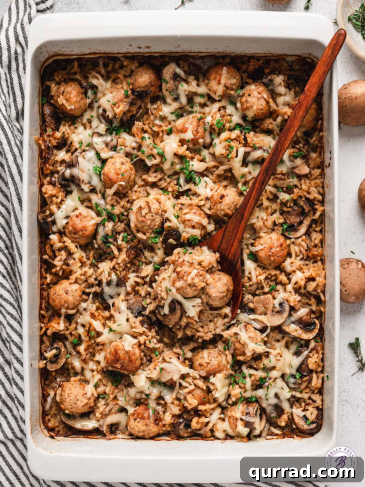 A wooden spoon in a French onion meatballs and rice casserole dish, ready to be served
