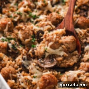 A wooden spoon scooping French onion meatballs and rice from a baking dish