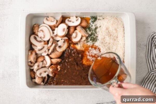 Pouring beef broth over sliced onions and rice in a baking dish