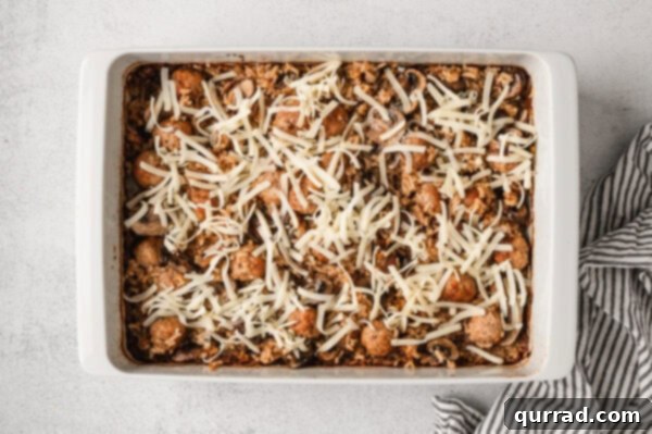 Overhead view of shredded cheese on top of French onion meatballs and rice, just out of the oven