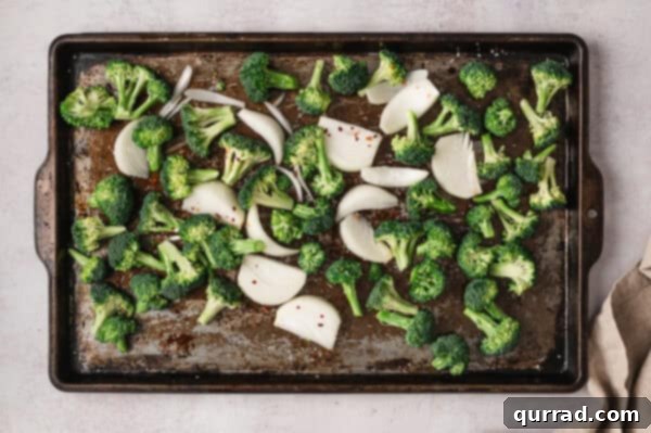 Effortless Sheet Pan Beef and Broccoli 4 Broccoli and onion wedges seasoned on a sheet pan, ready for roasting.