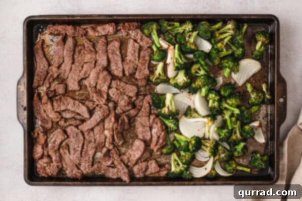 Effortless Sheet Pan Beef and Broccoli 6 Cooked slices of steak on a sheet pan with perfectly roasted broccoli and onion.