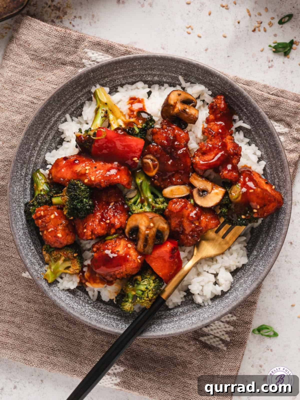 With pieces of breaded chicken, peppers, mushrooms, and broccoli, this Sheet Pan General Tso's Chicken makes a quick, easy dinner. A plate of sheet pan General Tso's chicken over rice, garnished