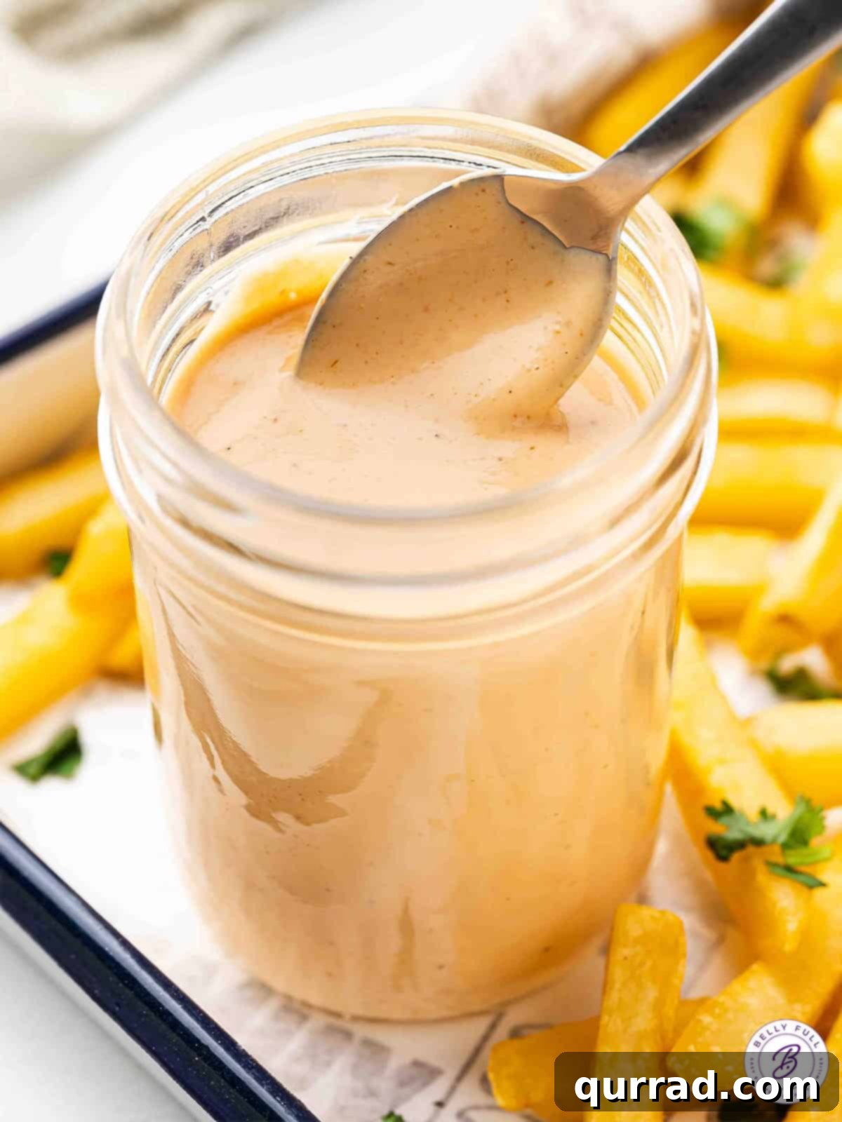 The Encore Sauce 2 Overhead view of a spoon in a jar of comeback sauce, showcasing its creamy texture and vibrant color.
