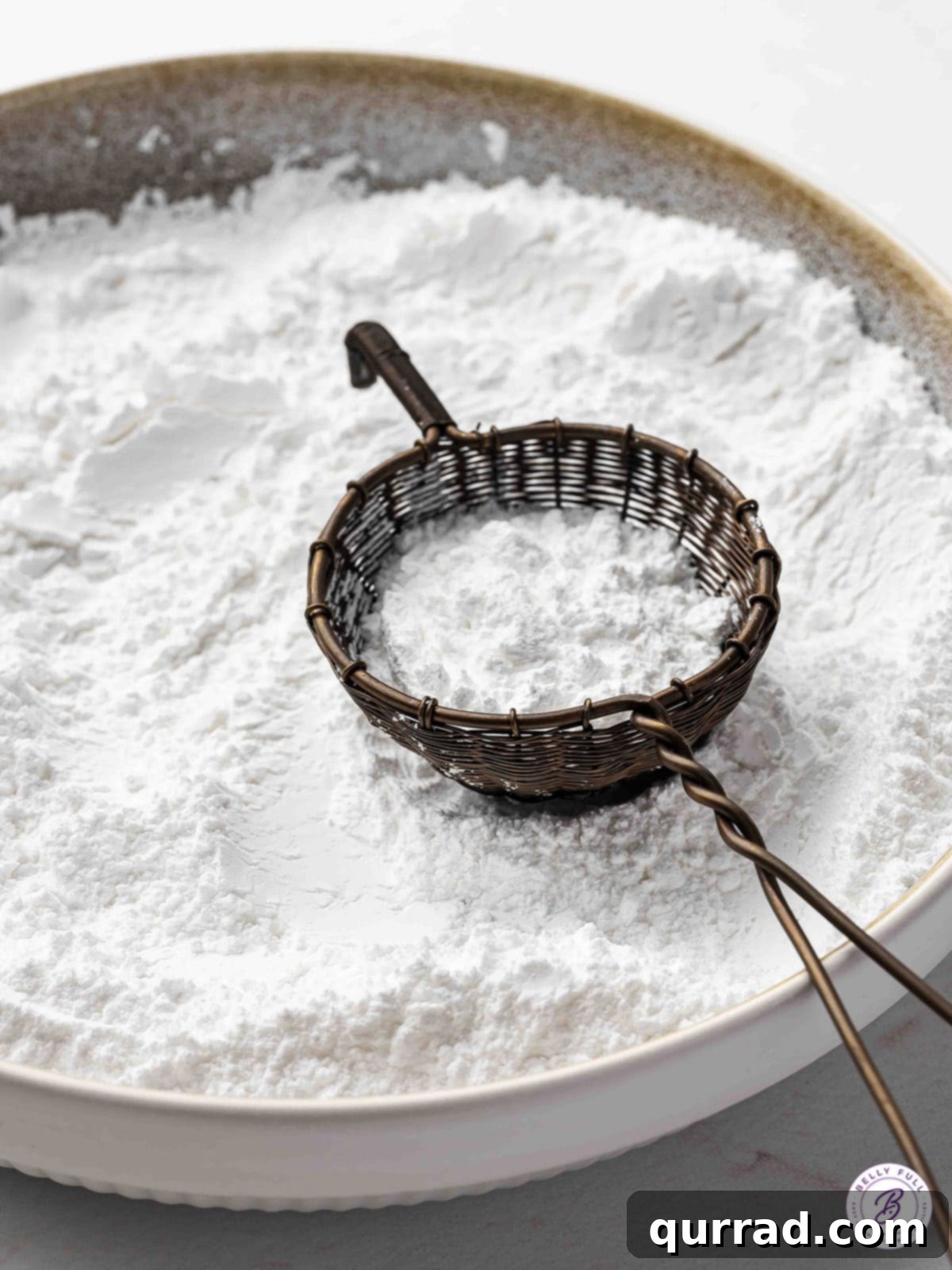 Sifting powdered sugar through a fine-mesh sieve into a bowl.