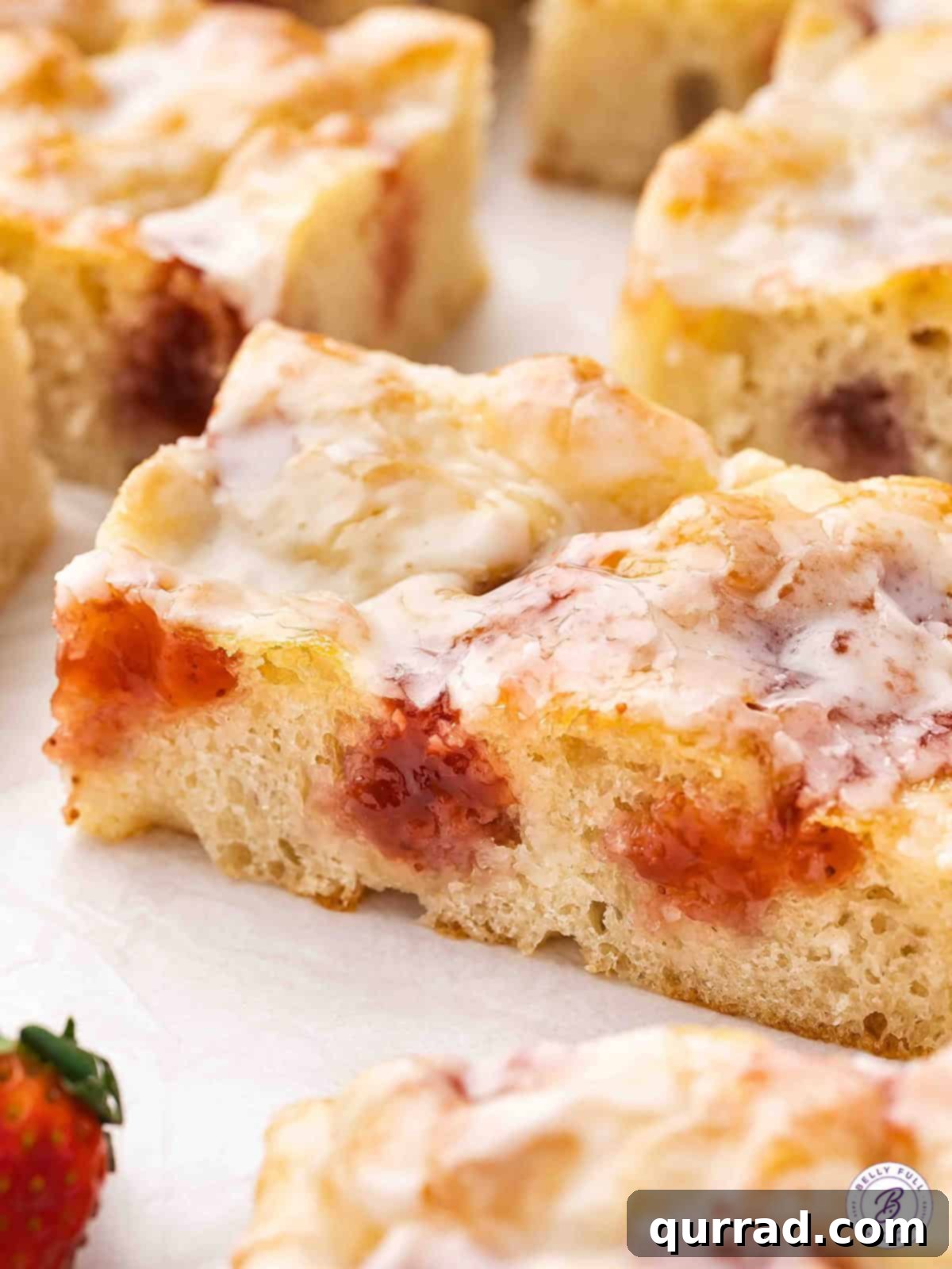 Soft focaccia bread is infused with strawberry jam and topped with a yummy glaze in this Jelly Donut Focaccia recipe. Super easy to make! A close-up view of individual slices of Jelly Donut Focaccia, showing the jam filling and glossy glaze