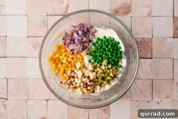 A bowl with mayo, onions, peas, corn, and gherkins