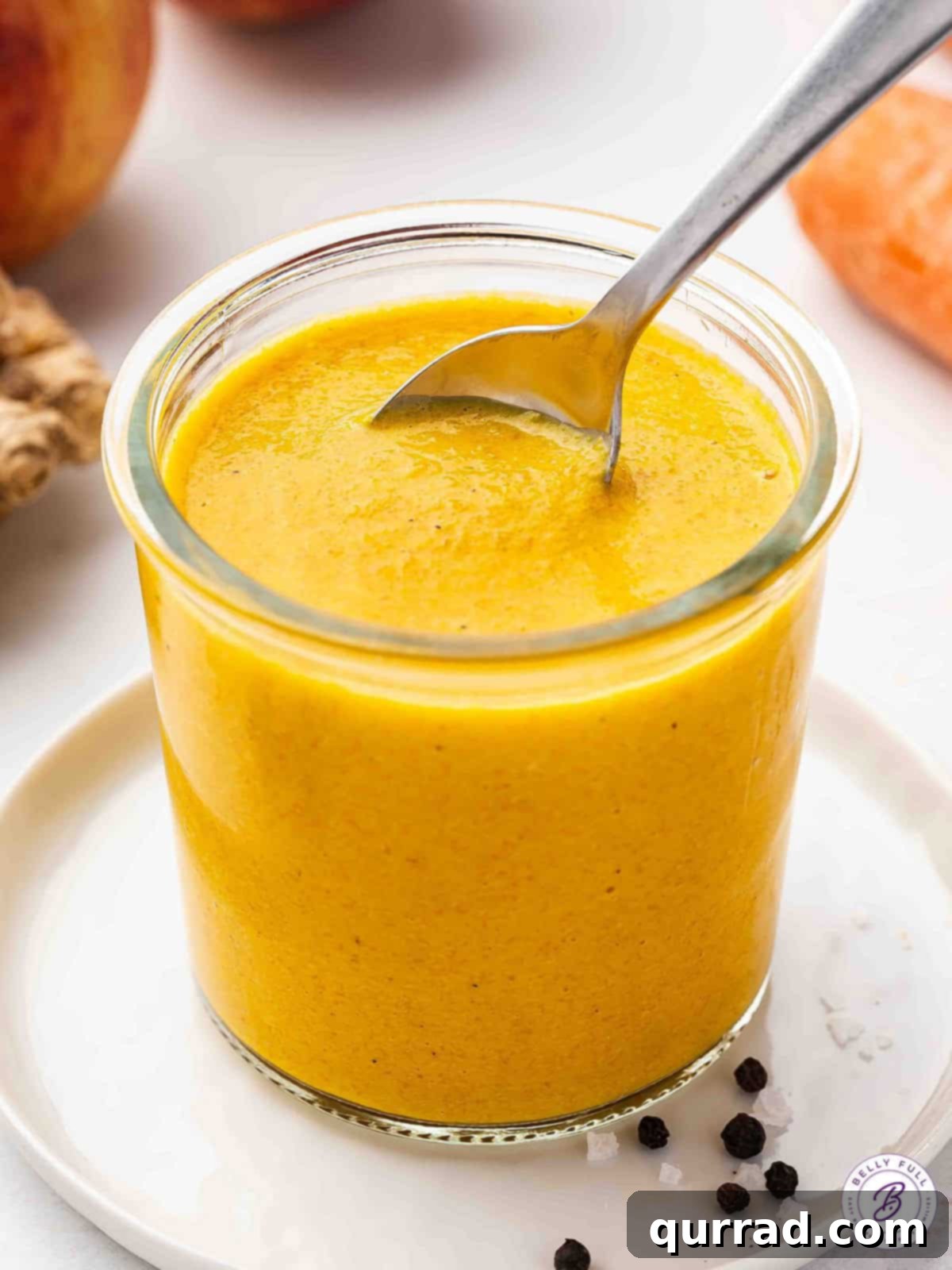 Tangy, Zesty & Creamy Carrot-Ginger Dressing Made with Fresh Carrots, Ginger, Apple, and Onion. Perfect for Salads, Bowls, and More! A spoon in a glass jar of homemade Carrot-Ginger dressing, showcasing its vibrant orange color