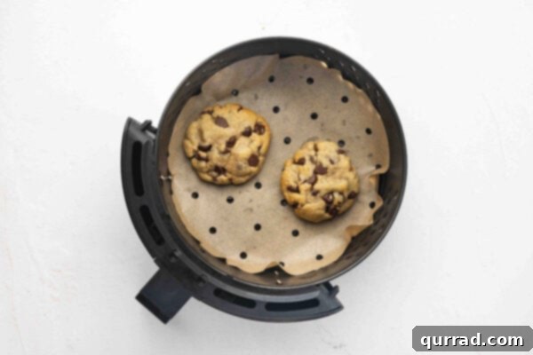 Two freshly baked single serve chocolate chip cookies in the air fryer basket