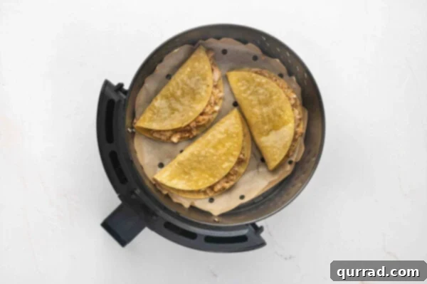 Three chicken tacos neatly arranged in a single layer within an air fryer basket, ready for cooking.