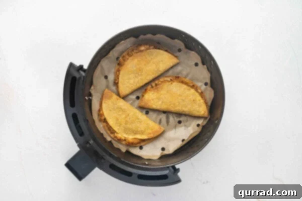 Three golden-brown, crispy chicken tacos cooking in the air fryer, halfway through the process.