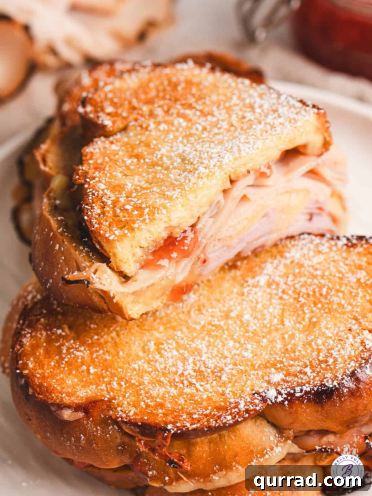 A half of a Monte Cristo grilled cheese on top of another one, showcasing the layers of ham, turkey, cheese, jam, and mustard