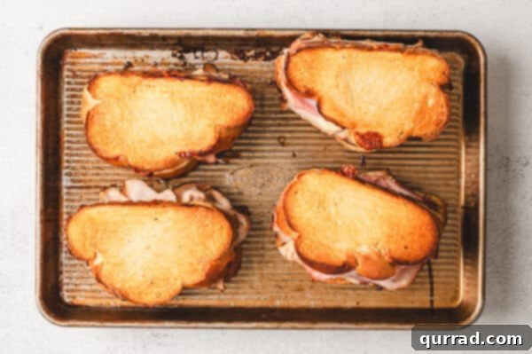 Overhead view of four Monte Cristo grilled cheese sandwiches baking on a sheet pan, golden and bubbling