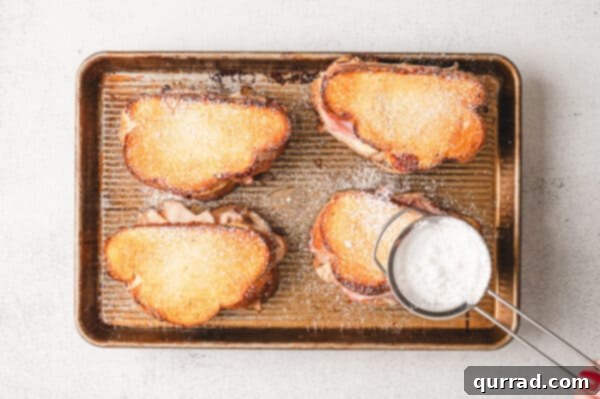 Dusting baked Monte Cristo grilled cheese sandwiches with powdered sugar