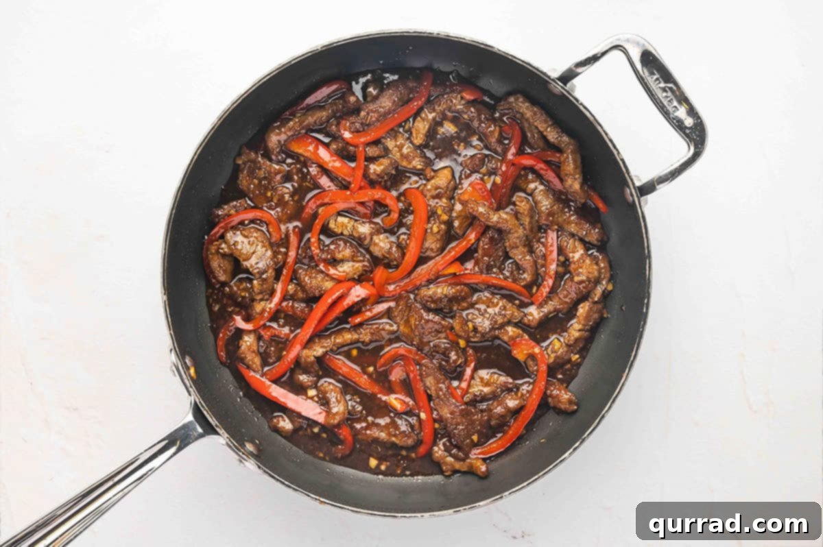 Seared flank steak and red peppers in a skillet, with sauce being poured over