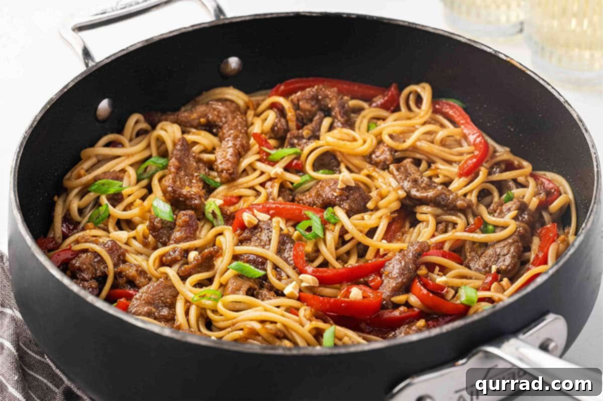 Side view of a skillet of Mongolian beef noodles, garnished with scallions and peanuts