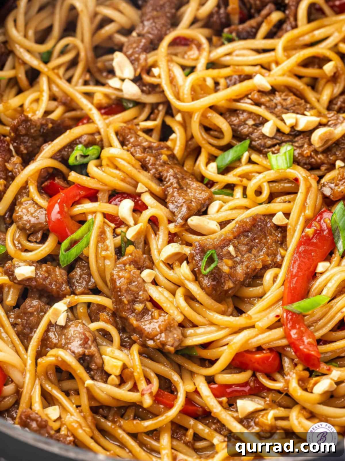 Overhead view of Mongolian beef noodles garnished with fresh scallions and crushed peanuts in a large bowl