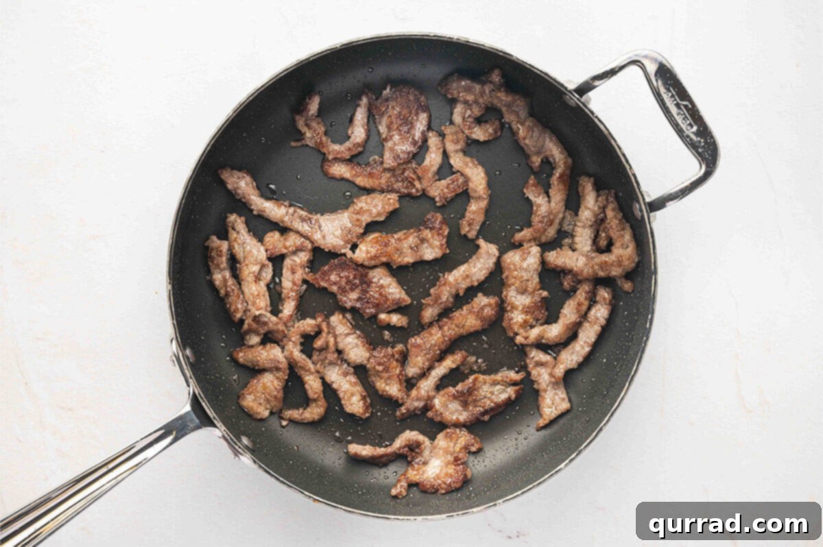 Strips of seared flank steak sizzling in a skillet