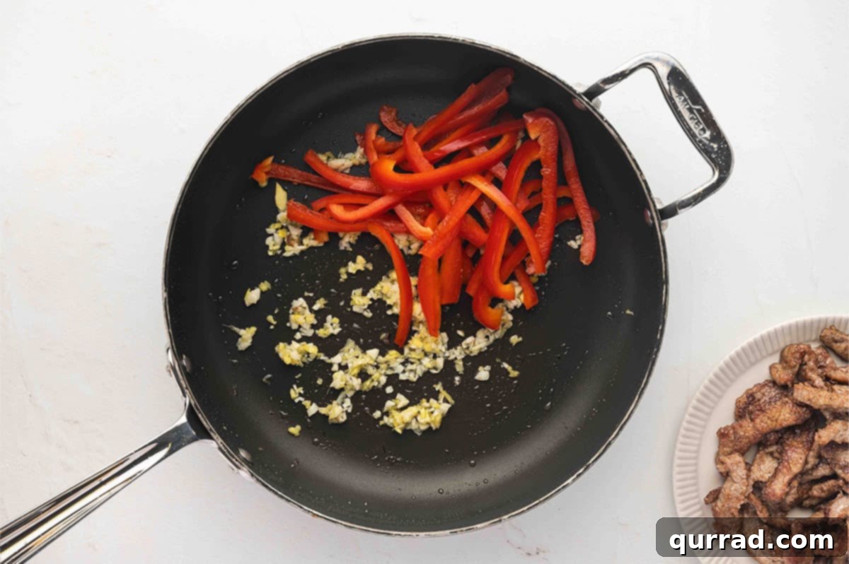 Minced garlic, grated ginger, and sliced red bell pepper cooking in a skillet
