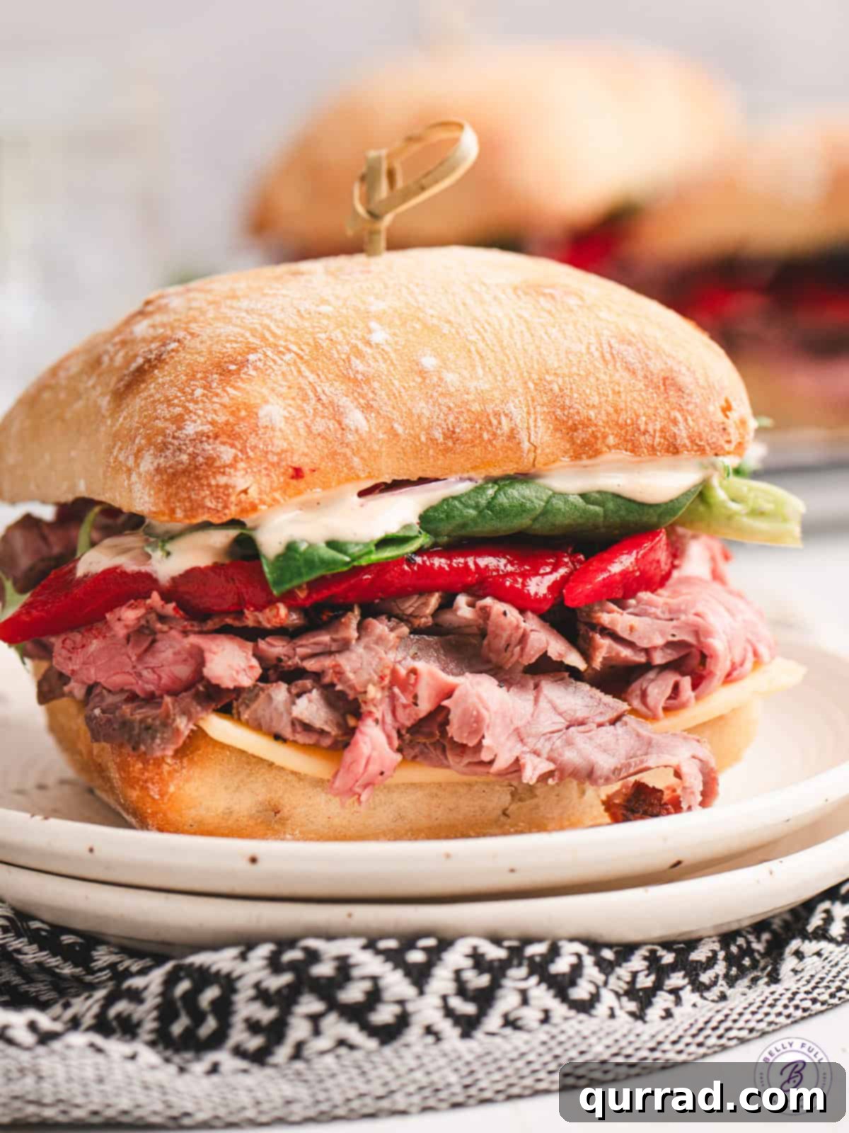The ultimate El Matador Sandwich: toasted ciabatta, spicy chipotle aioli, tender tri-tip, smoked Gouda, and vibrant roasted red peppers. A visually stunning El Matador Sandwich with all its layers visible, served on a white plate, highlighting its gourmet appeal.