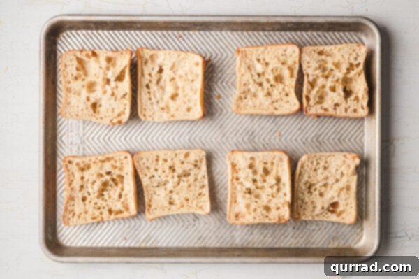 Sliced ciabatta rolls baking on a sheet pan