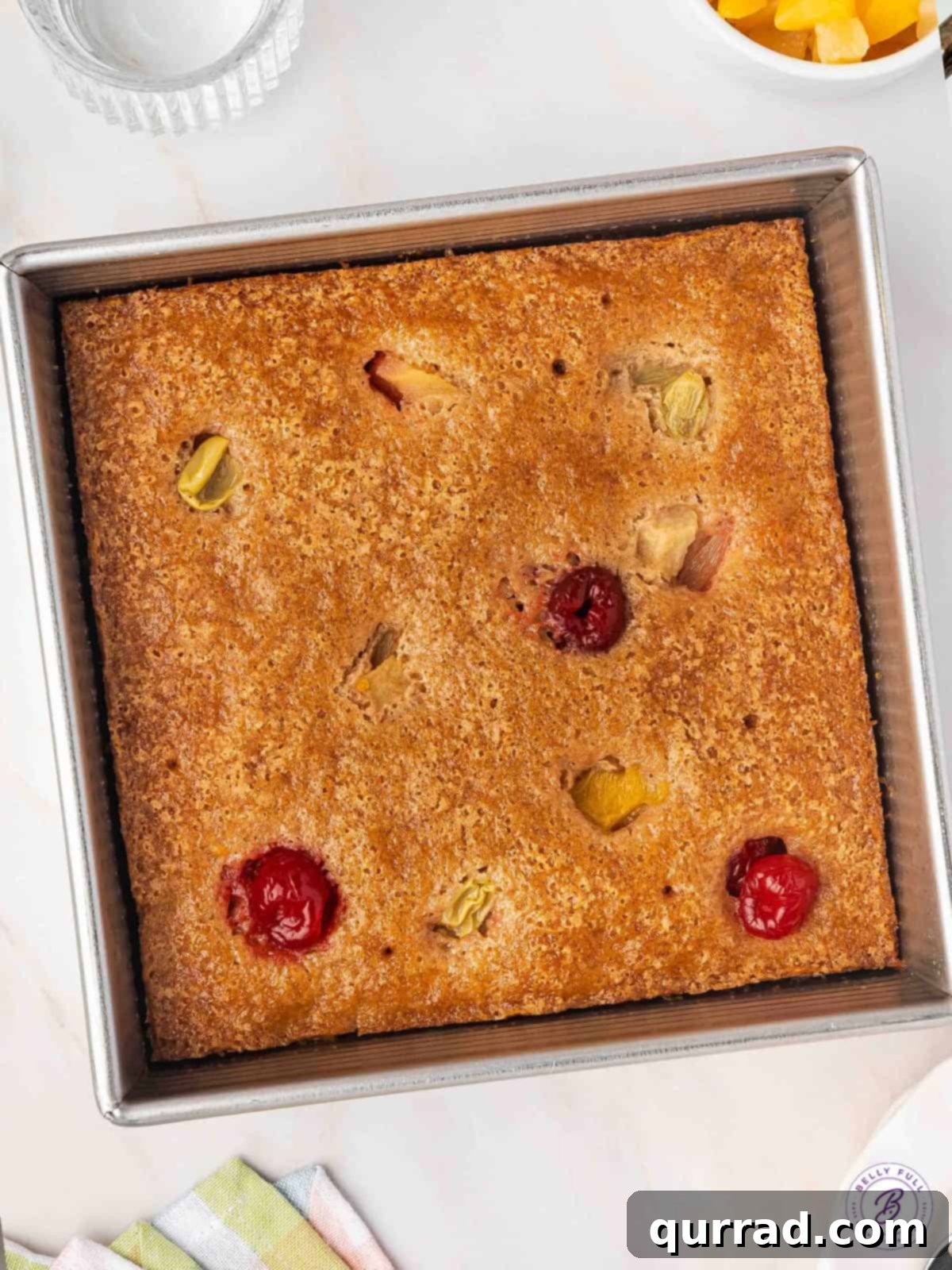 Cuppa Cake Delight 2 Golden-brown Cuppa Cuppa Cake in a square baking pan, ready to be served, showcasing its moist texture and fruit pieces.