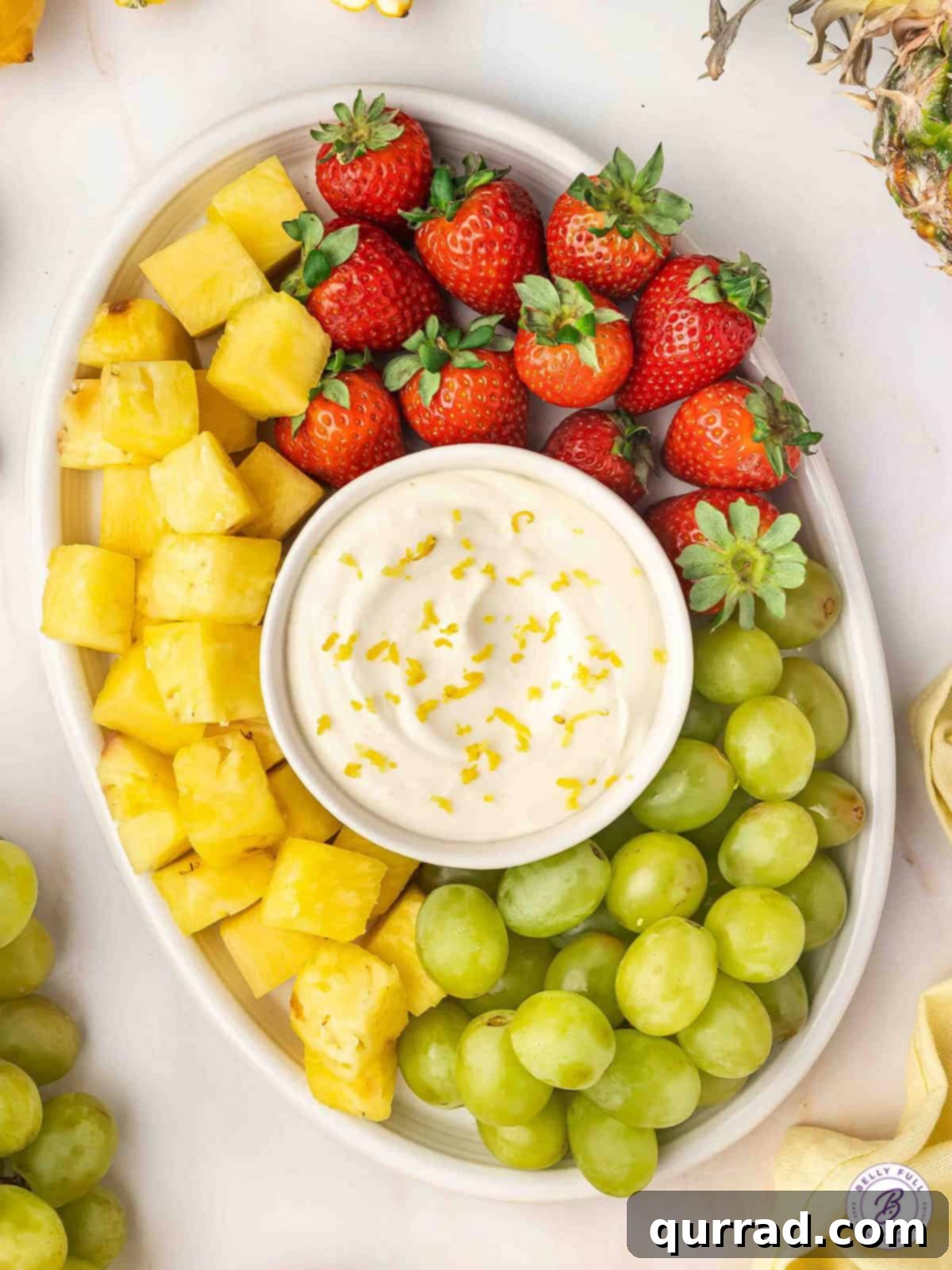 Ready in just 5 minutes, this Lemonade Fruit Dip is sweet, tangy, and delightfully delicious! Serve with a variety of fruits. Overhead view of a vibrant lemonade fruit dip artfully arranged on a platter, surrounded by fresh strawberries, golden pineapple chunks, and bright green grapes.