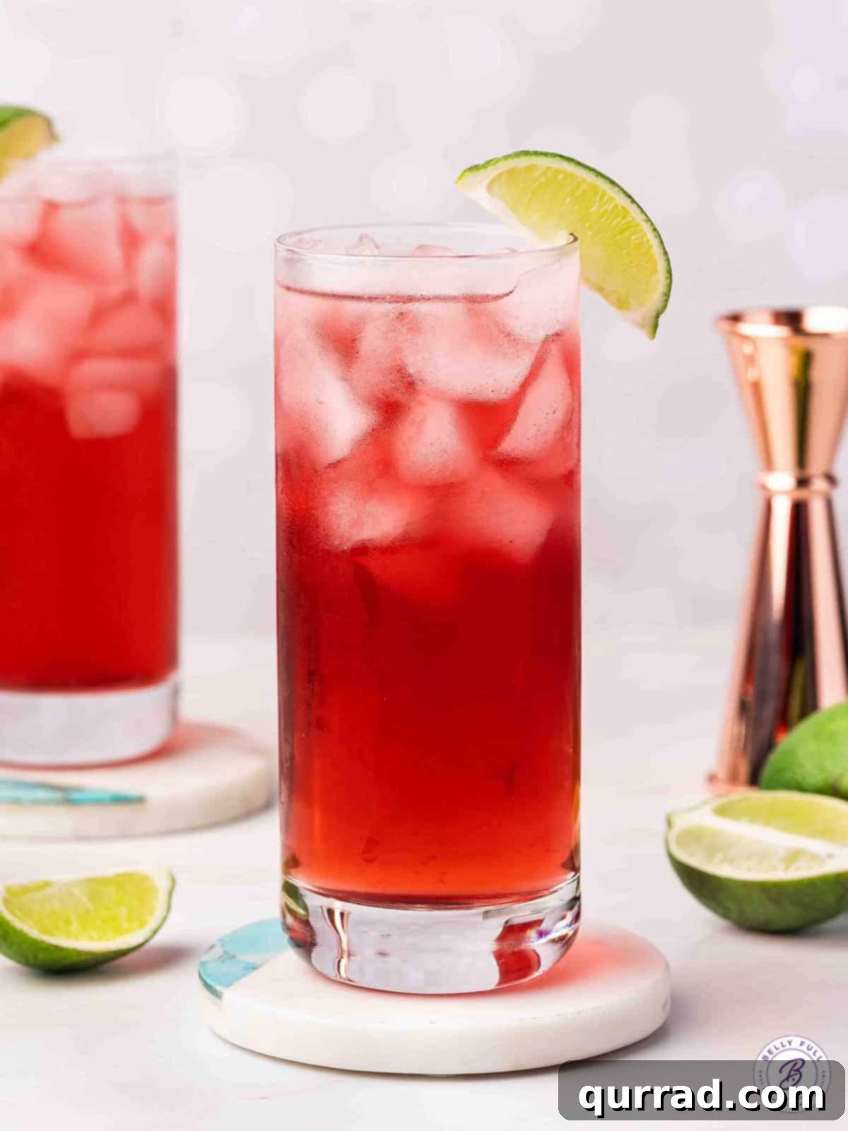 A vibrant red Woo Woo cocktail, garnished with a lime wedge, resting on a coaster, ready to be enjoyed.