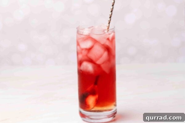 A bar spoon stirring a vibrant Woo Woo cocktail in a glass, mixing the spirits and juice.