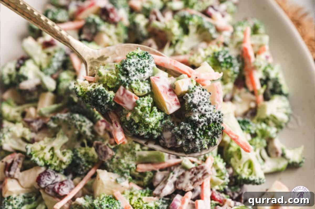 A wooden spoon serving a portion of vibrant Broccoli Apple Salad from a large bowl, highlighting its fresh ingredients and creamy texture