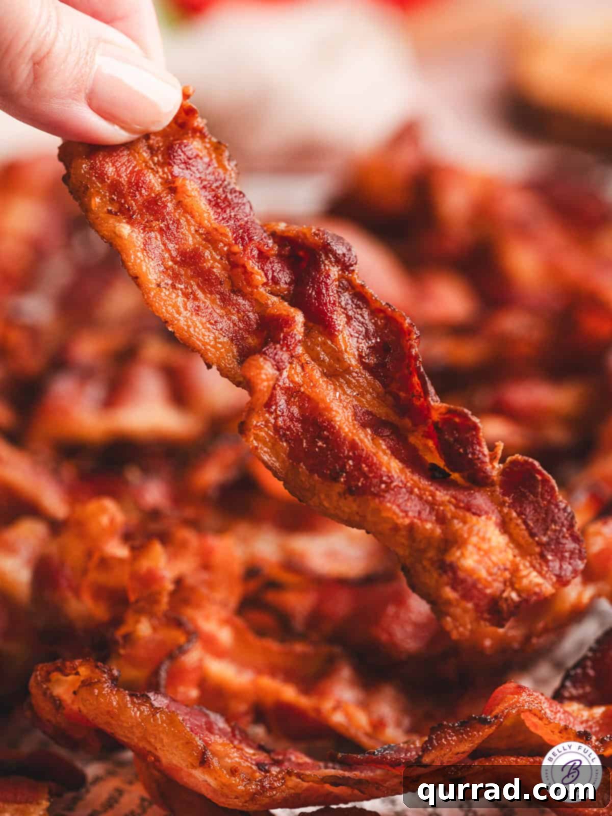Crispy Air Fryer Bacon Perfection 7 A hand gracefully holds up a single, perfectly crispy strip of air fryer bacon, showcasing its golden-brown texture.