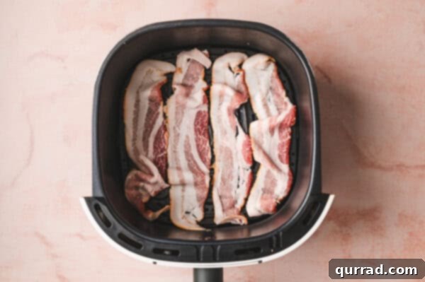 Slices of uncooked bacon arranged in a single layer in the air fryer basket.