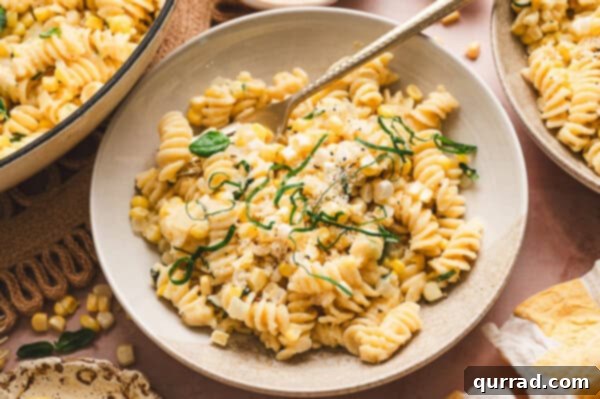 A beautifully plated dish of creamy corn pasta, garnished with fresh basil and Parmesan.