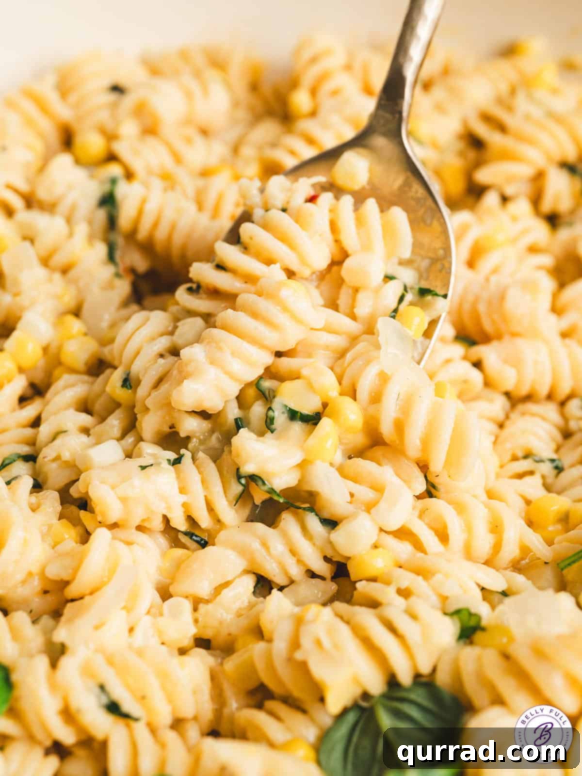 Close up of a spoon stirring creamy corn pasta, showing the rich sauce and corn kernels.